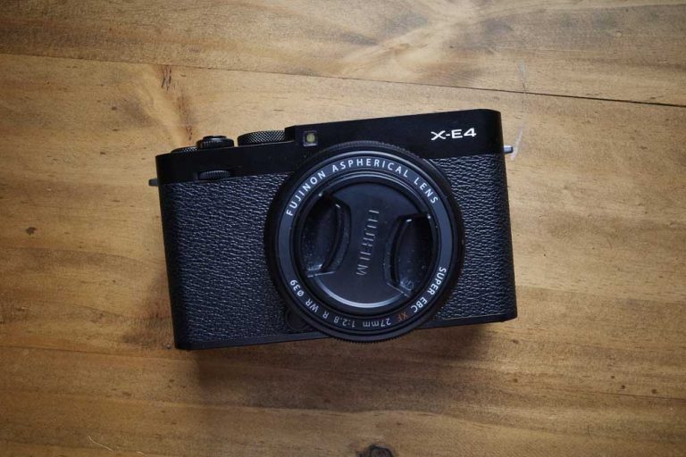 The Fujifilm X-E4 on a wood table from above.