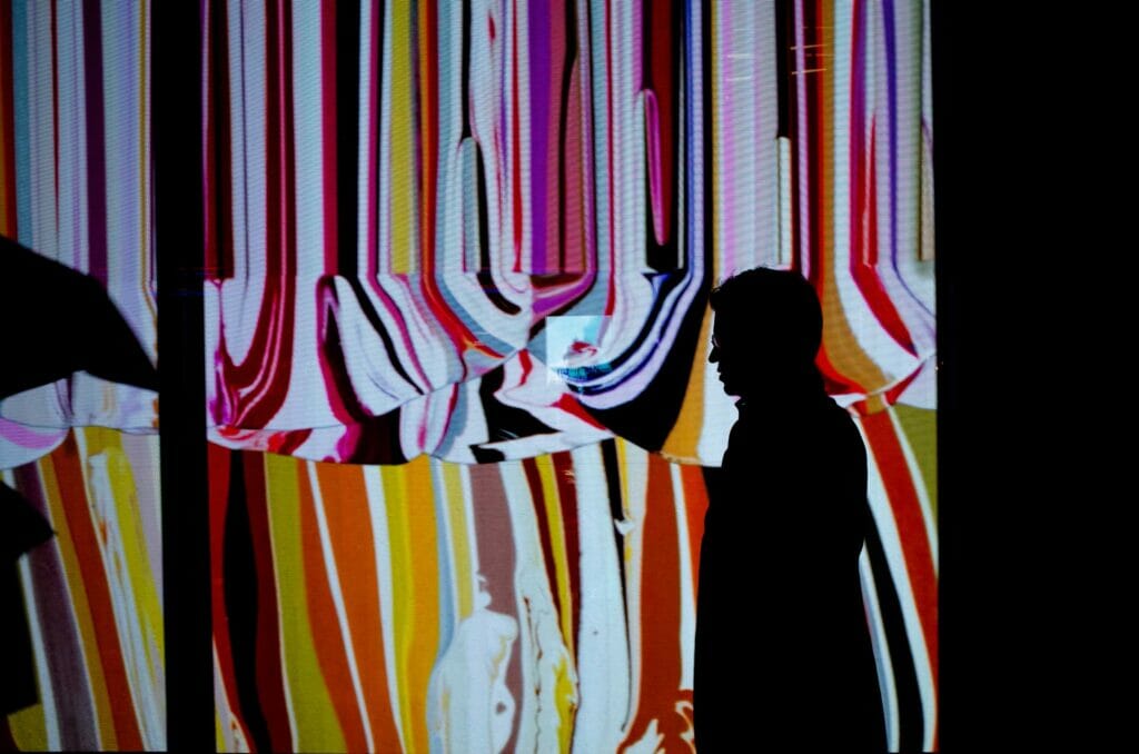 A silhouette of a man with glasses against a colorful background with vertical lines.