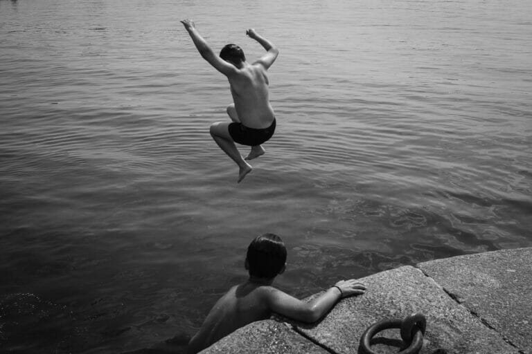 Two boys jumping off a platform into water.
